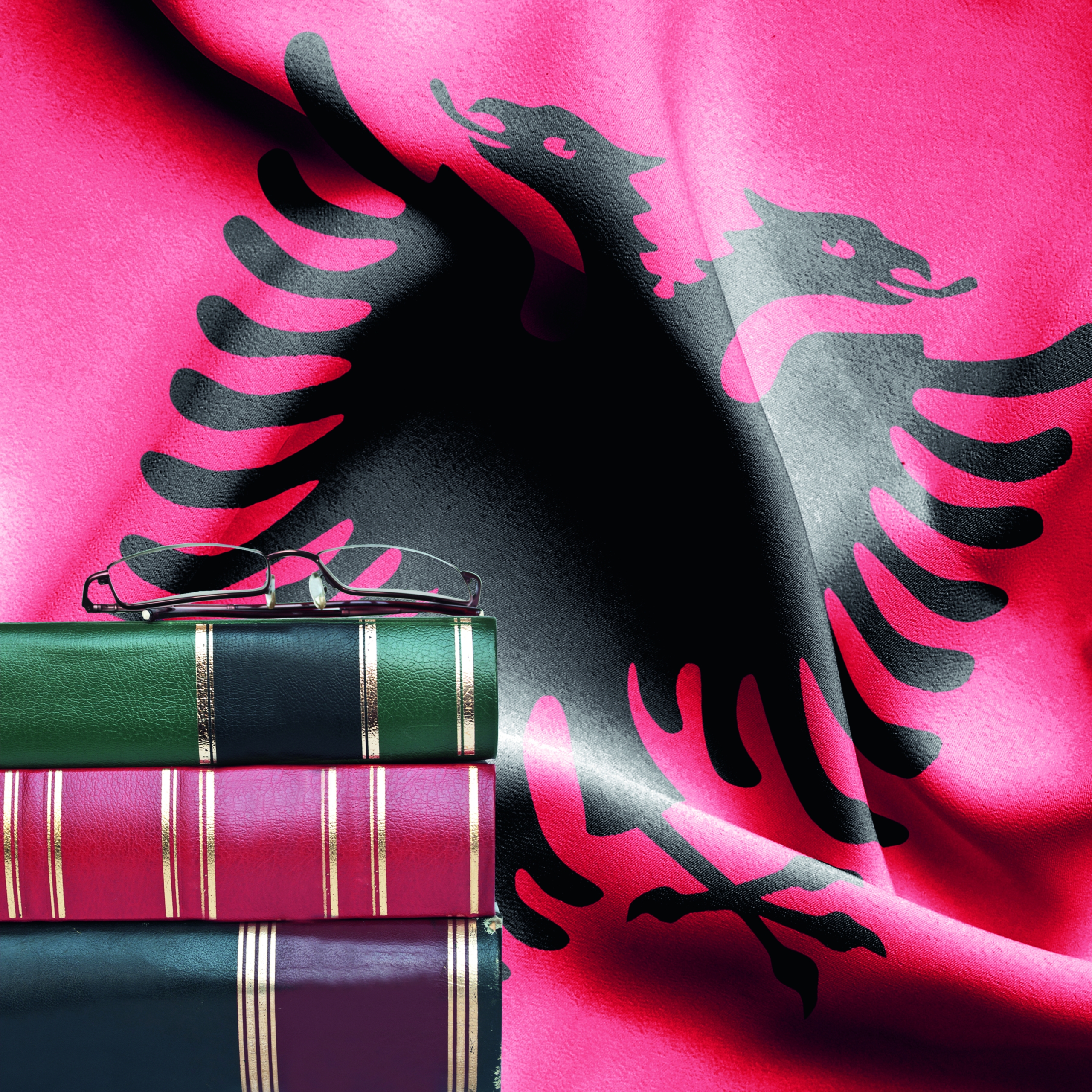 Education concept - Stack of books and reading glasses against National flag of Albania