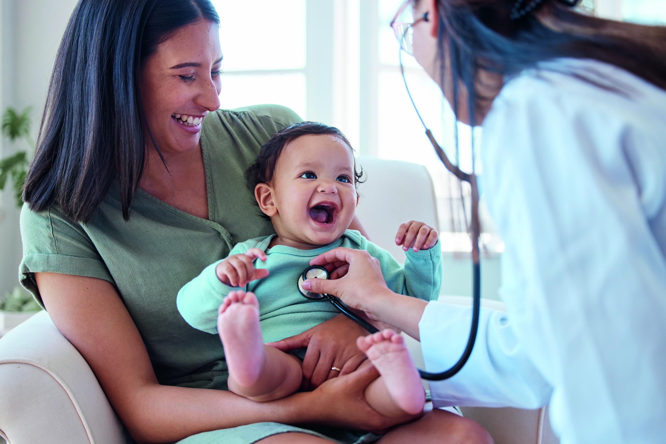 Shot of a baby sitting on her mother's lap while being examined by a doctor