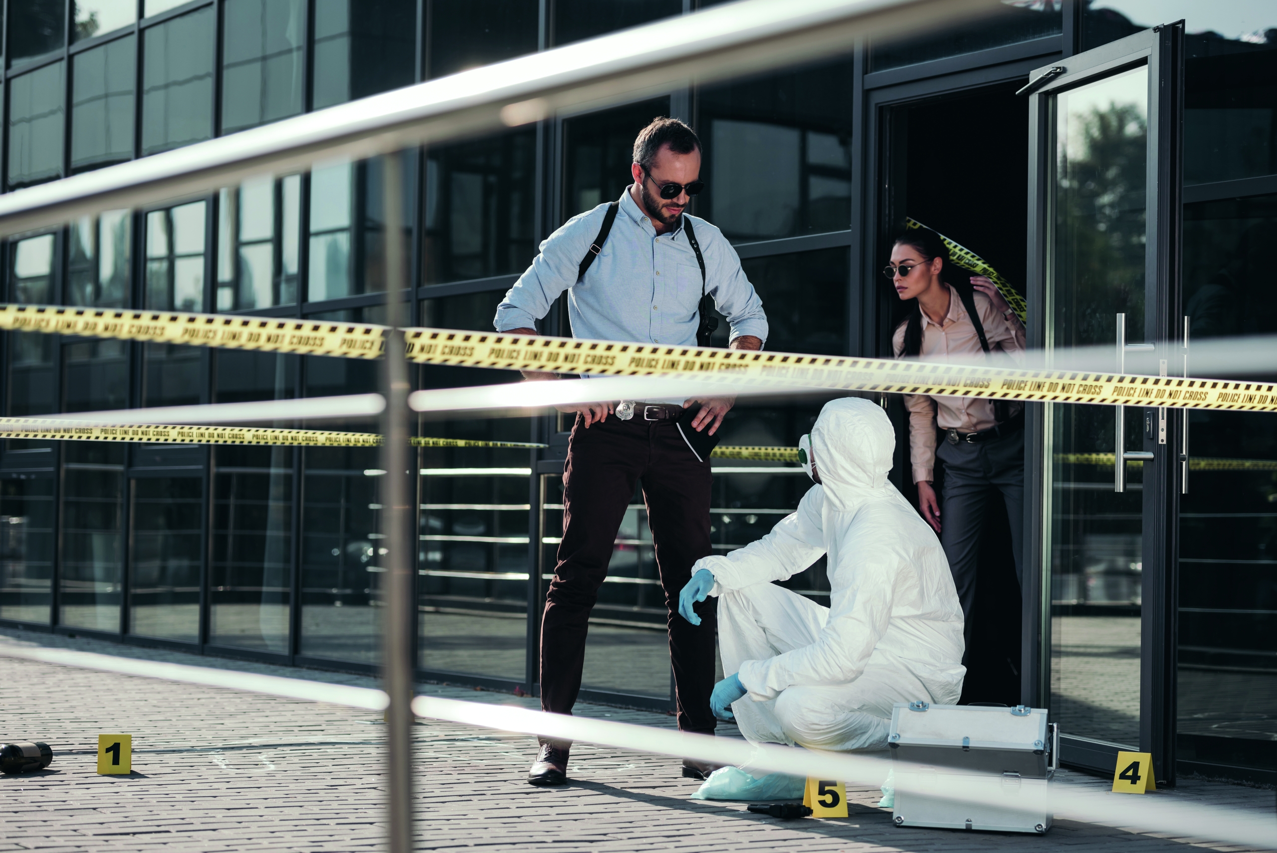 detectives and criminologist in protective suit and latex gloves communicating at crime scene