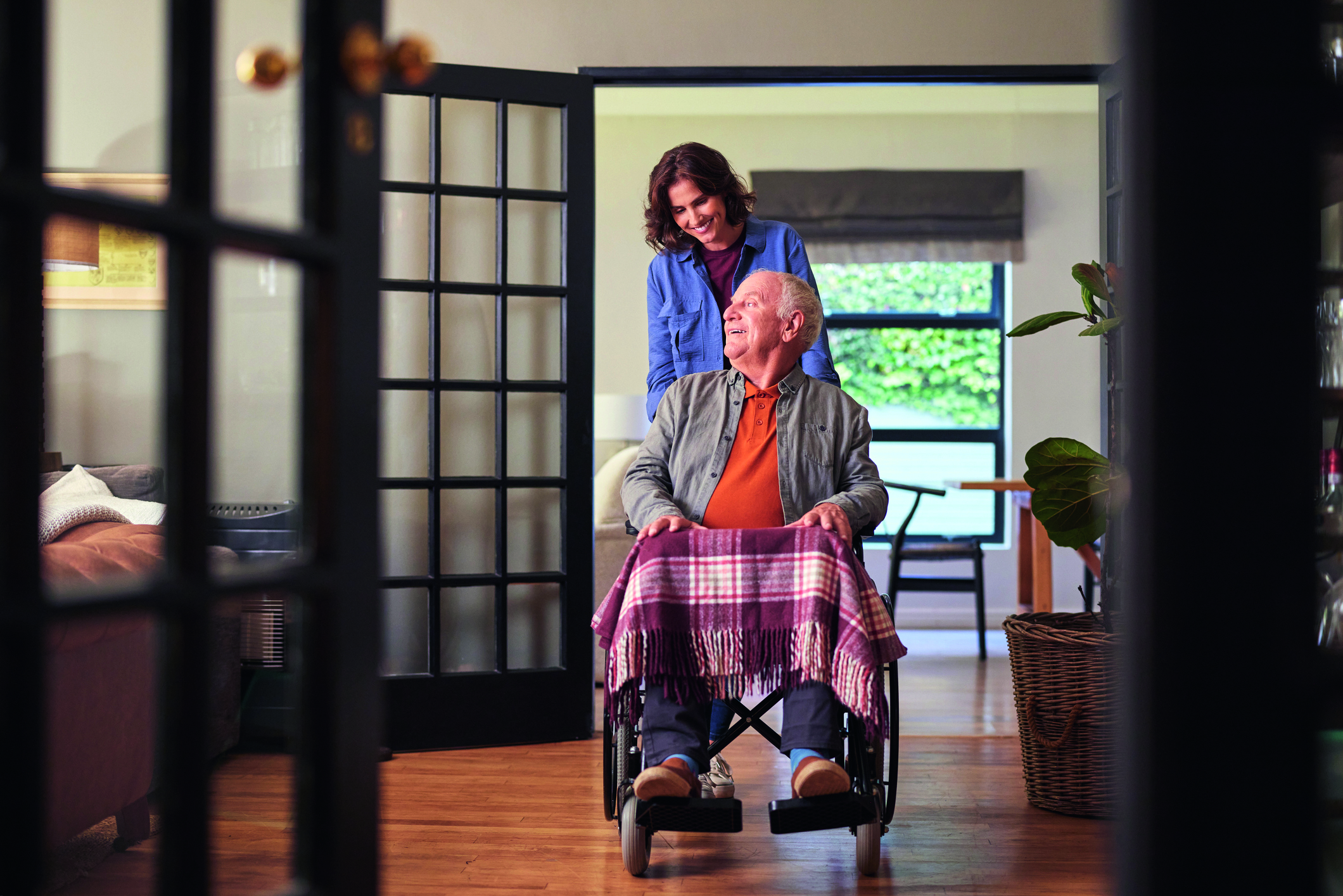 Senior man in wheelchair pushed by smiling woman